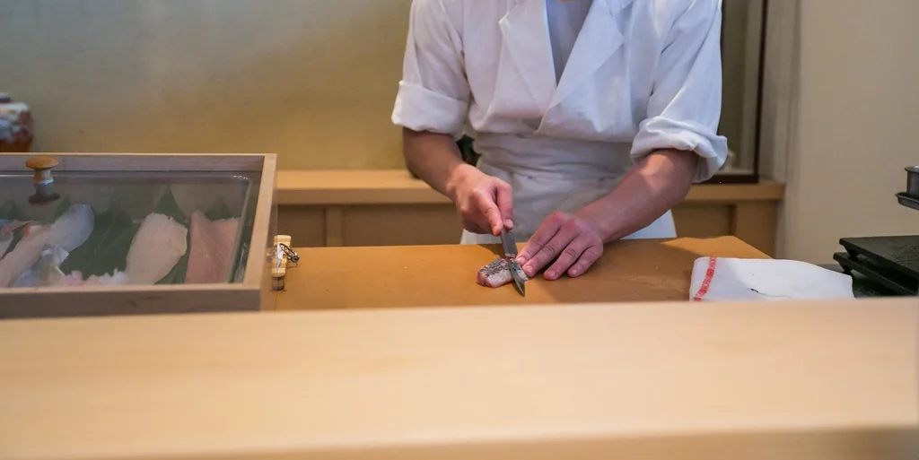 A chef slices fish on a pale wooden counter in a calm kitchen